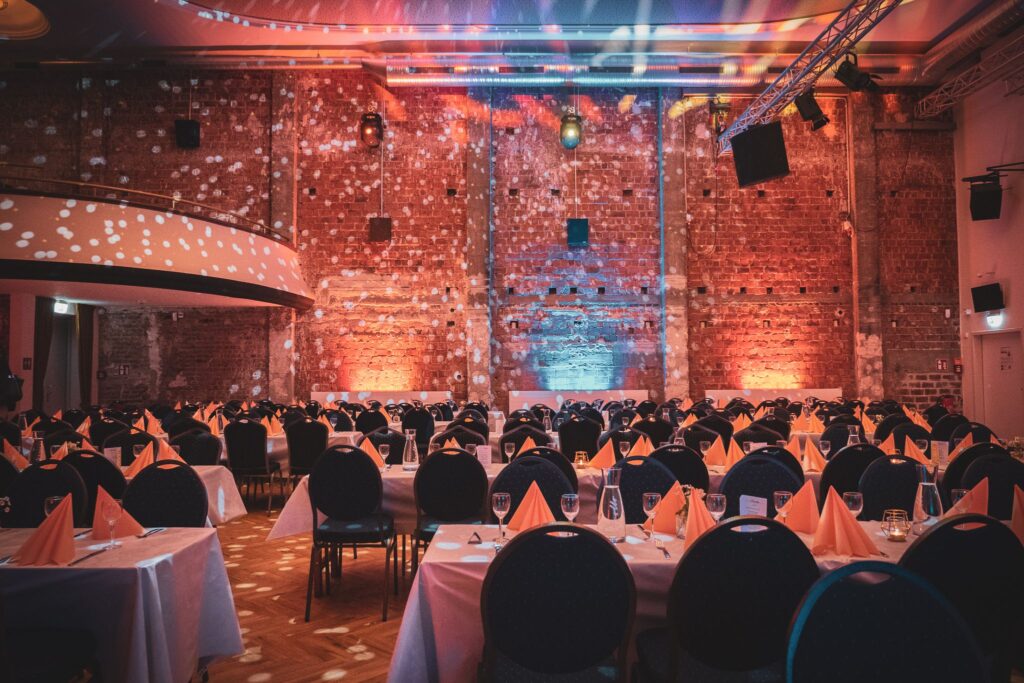 Festlich gedeckter Veranstaltungssaal mit Backsteinwand, stimmungsvoller Beleuchtung und elegant arrangierten Tischen.