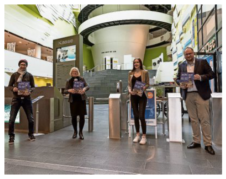 Zwei Frauen und zwei Männer posieren in einem Foyer und präsentieren ein Magazin, das sie in den Händen halten.