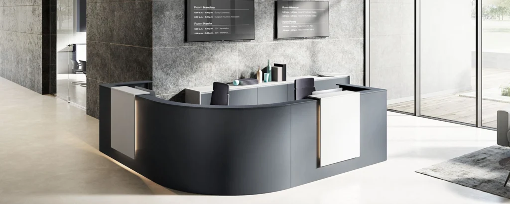 Moderner Empfangsbereich mit halbrundem Tresen und grauer Wandgestaltung in einem Bürogebäude.