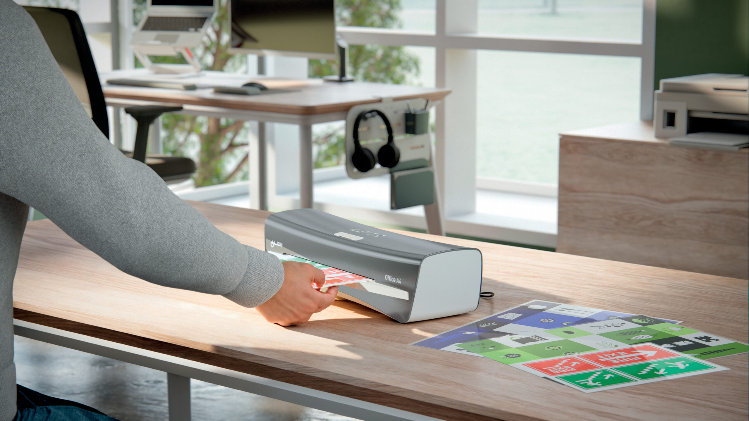 Person laminiert farbige Dokumente mit einem A4-Laminiergerät auf einem Schreibtisch in einem modernen Büro mit Tageslicht.