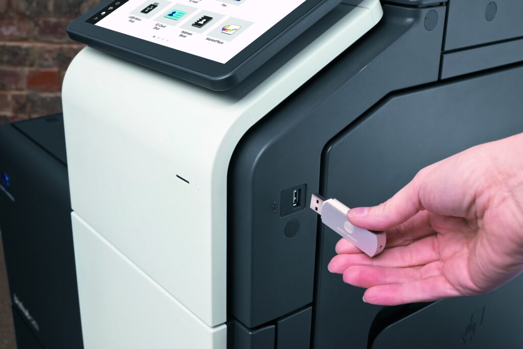 Hand steckt einen USB-Stick in den Anschluss eines modernen Multifunktionsdruckers mit Touchscreen-Bedienfeld.