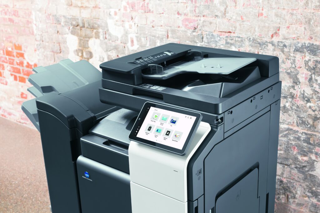 Moderner Multifunktionsdrucker mit großem Touchdisplay vor einer Backsteinwand.