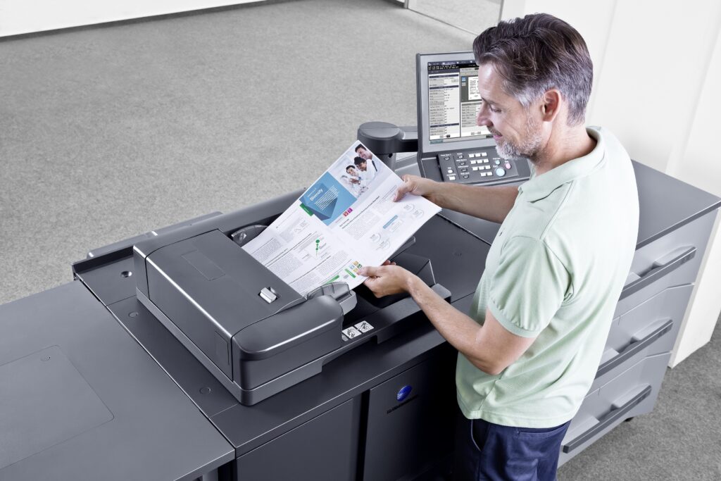 Mann überprüft frisch gedruckte Broschüre an großem professionellen Drucker im Büro.