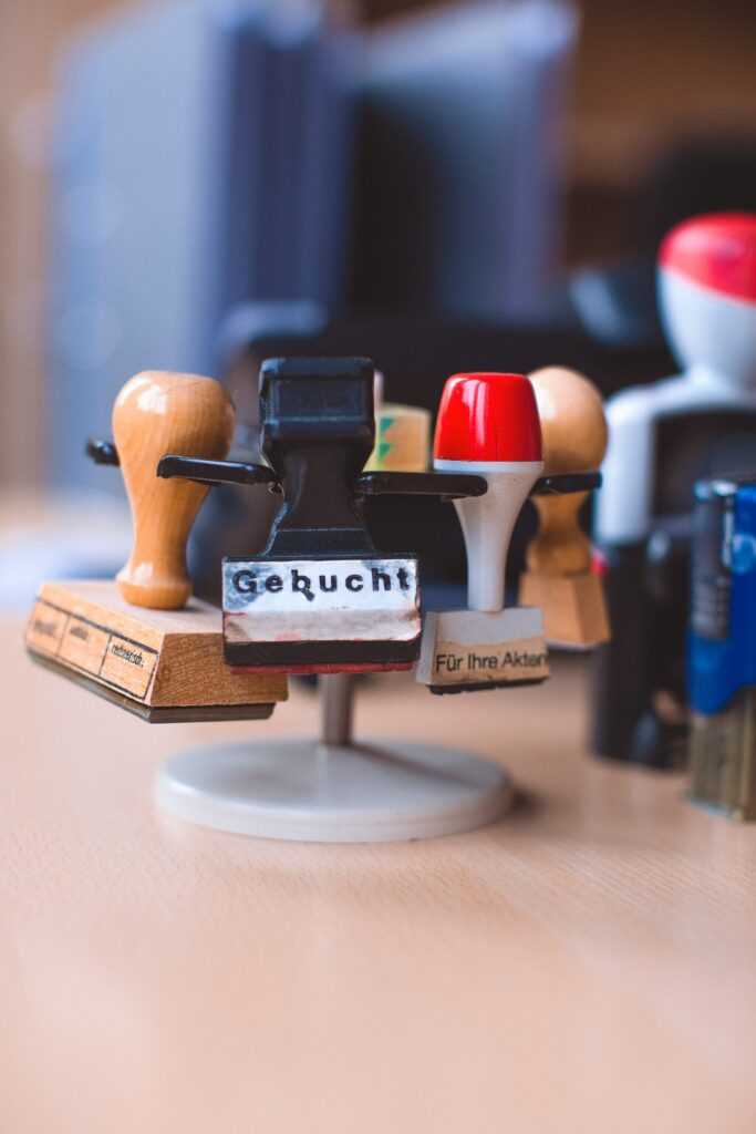 Mehrere Bürostempel in einem Stempelhalter auf einem Schreibtisch, einer mit der Aufschrift „Gebucht“.