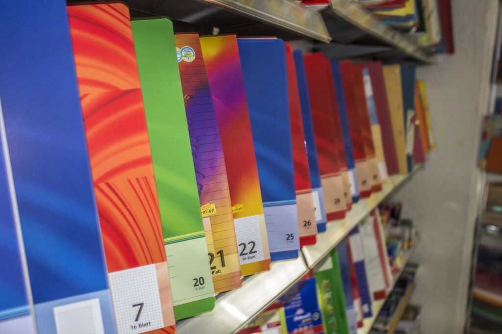 Bunte Schulhefte in verschiedenen Farben stehen sortiert im Regal eines Schreibwarenladens.